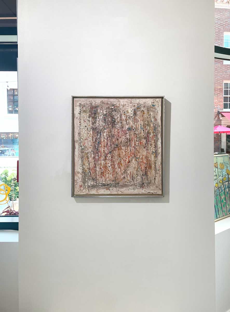 A white and multicolored abstract painting in a silver floater frame hangs on a white wall.
