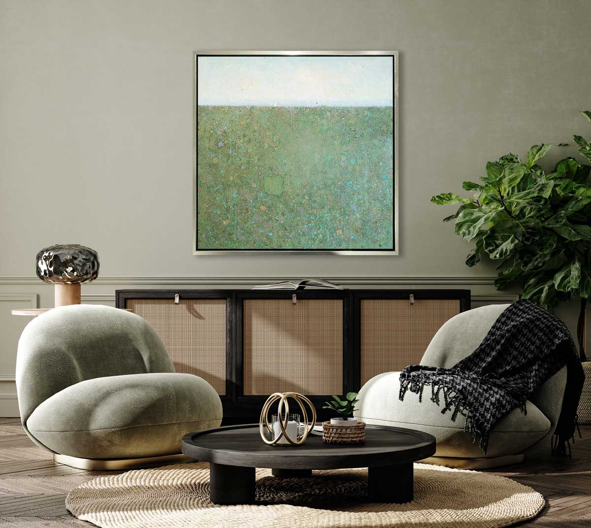 A green and blue abstract landscape in a silver floater frame hangs on a grey wall above a black crendeza, two low modern green chairs and a black round coffee table.