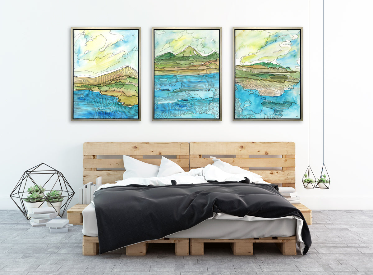 Three blue, green, brown and light yellow abstract landscapes with black outlines prints in silver floater frames hang side by side on a white wall above a palette framed bed, a wired hexagonal decoration with three potted succulents, stacks of books and two potted succulents hanging from wired decorations.