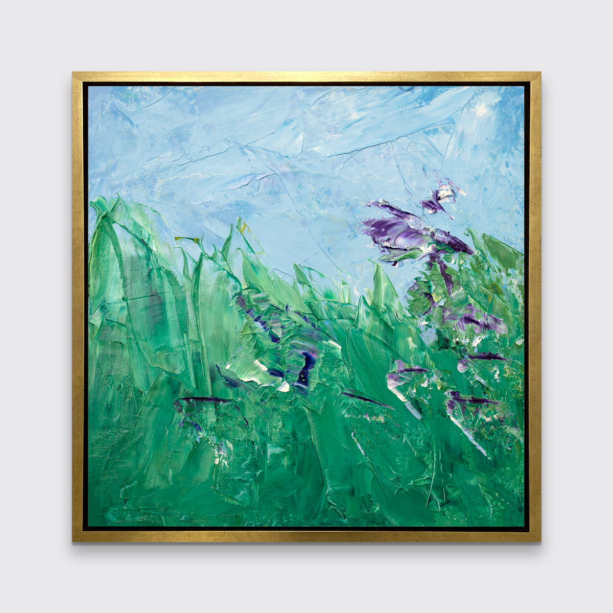 A blue, green and purple abstract landscape print in a gold floater frame hangs on a white wall.
