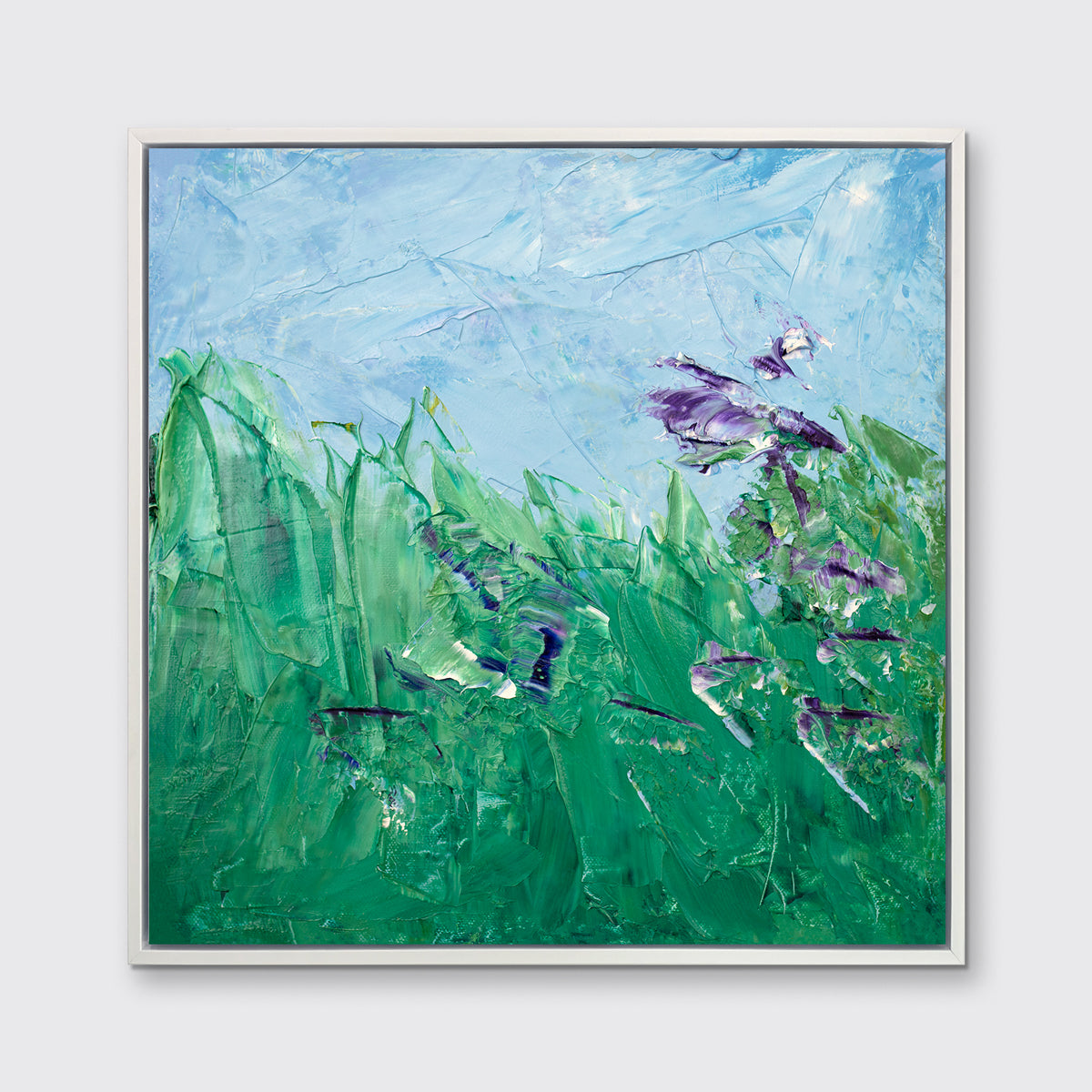 A blue, green and purple abstract landscape print in a white floater frame hangs on a white wall.