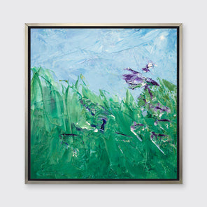 A blue, green and purple abstract landscape print in a silver floater frame hangs on a white wall.