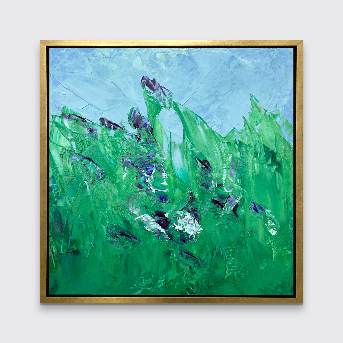 A blue and green abstract landscape print in a gold floater frame hangs on a white wall.