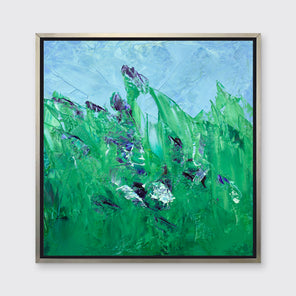 A blue and green abstract landscape print in a silver floater frame hangs on a white wall.