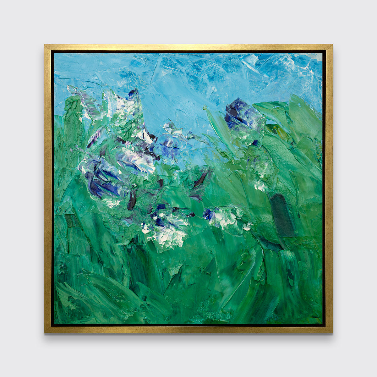 A blue, green, purple and white abstract landscape print in a gold floater frame hangs on a white wall.