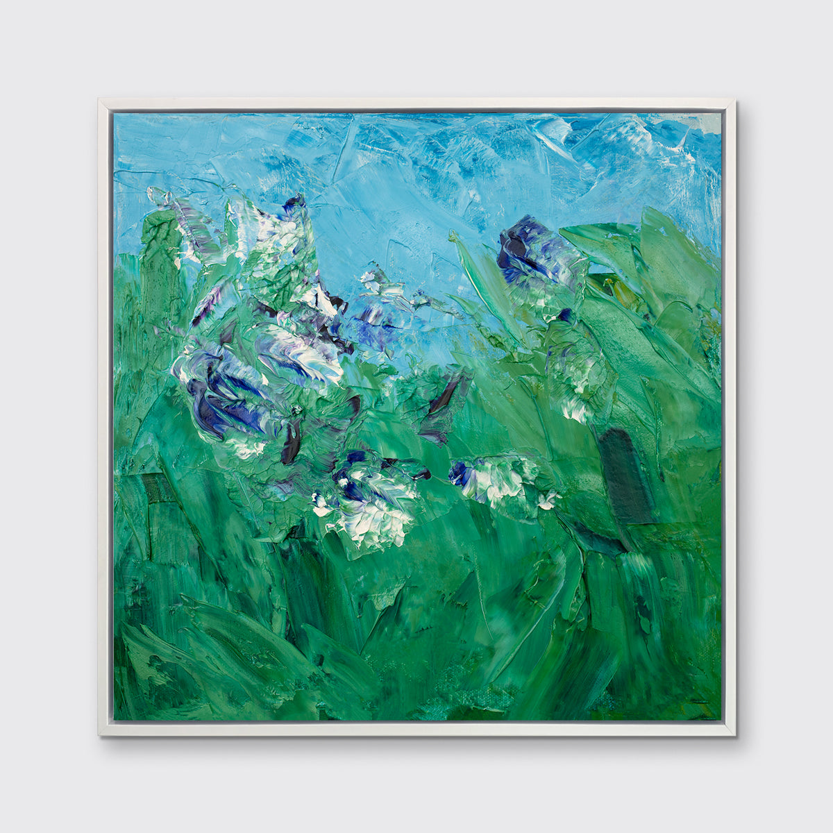 A blue, green, purple and white abstract landscape print in a white floater frame hangs on a white wall.