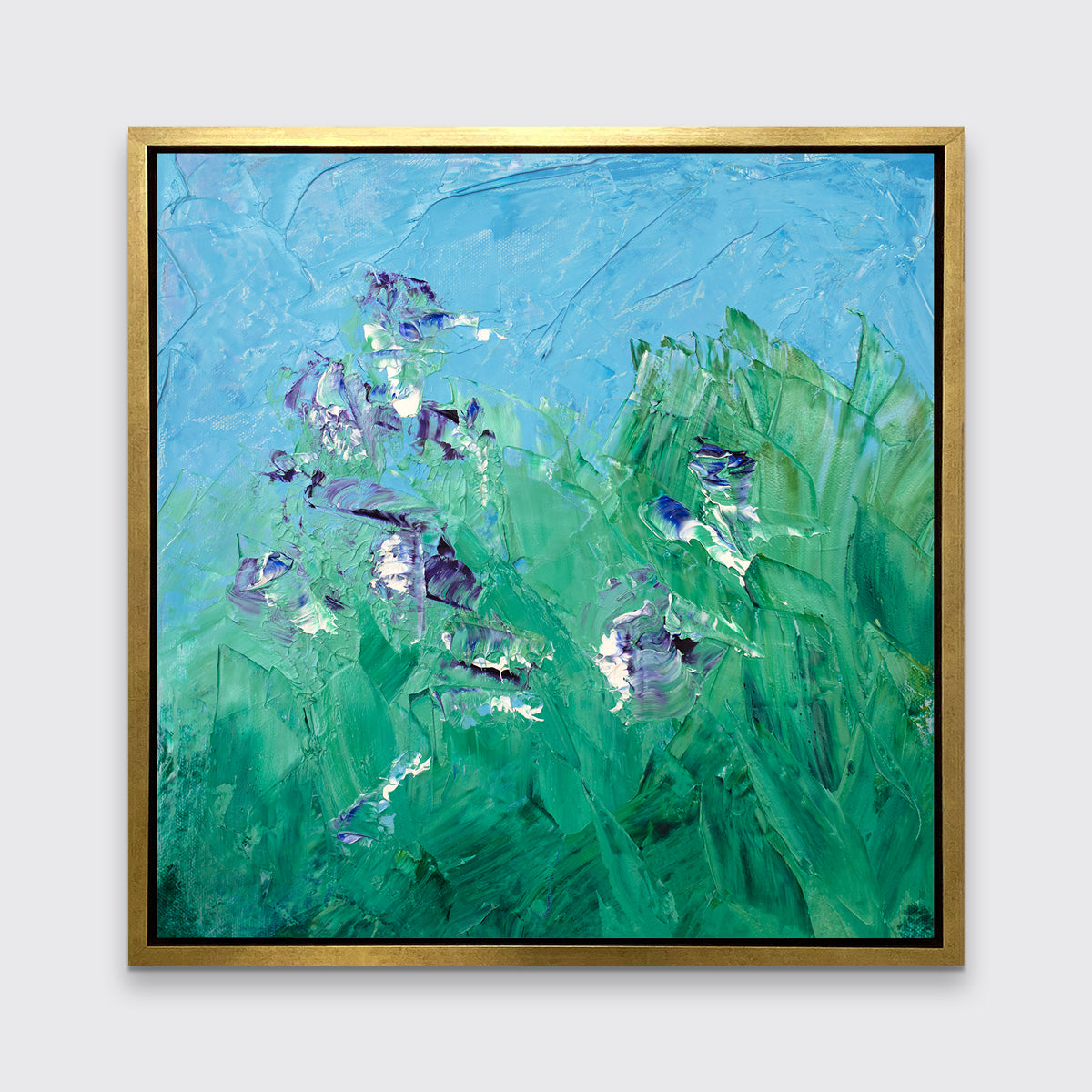 A blue, green, purple and white abstract landscape print in a gold floater frame hangs on a white wall.