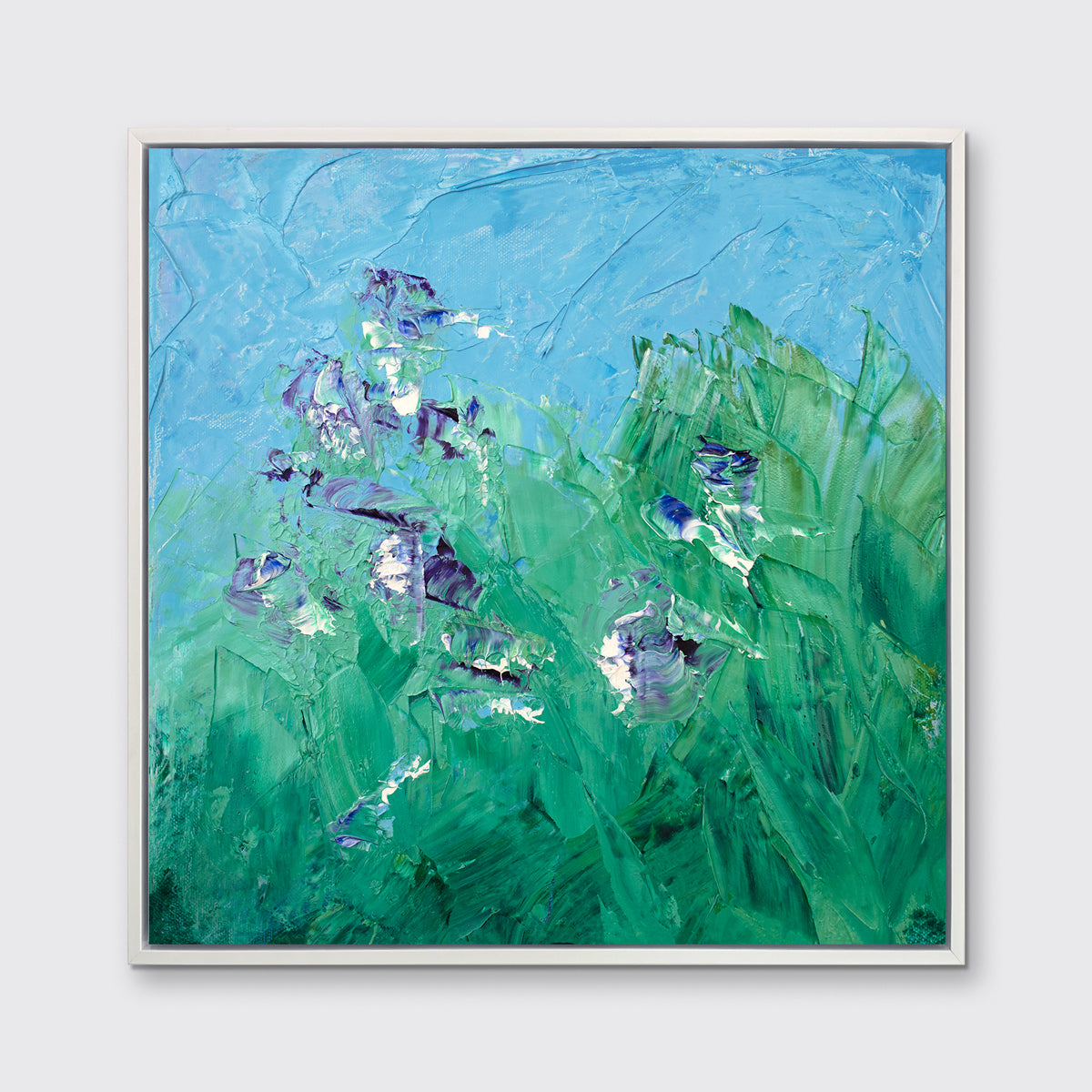 A blue, green, purple and white abstract landscape print in a white floater frame hangs on a white wall.