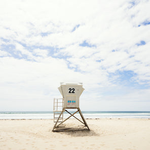 A rear view photograph of a beige lifeguard stand in front of a view of the ocean in San Diego, California. 
