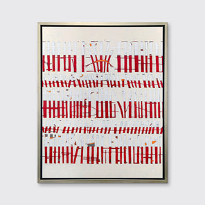 A beige, white and red abstract print in a silver floater frame hangs on a white wall.