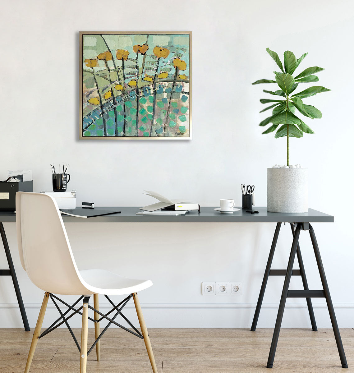 A floral abstract encaustic painting framed in a gold frame, hanging on a white wall above a modern grey desk, chair, office accessories and a potted plant. 