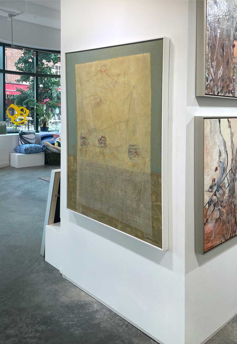 A right side-angle view of a teal, yellow and grey abstract painting in a white floater frame hangs on a white wall.