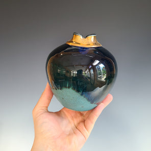 A blue and teal rounded ceramic vessel with a gold neck and a navy lip.