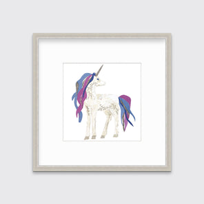 A white, purple, blue and silver collaged unicorn print in a silver frame with a mat hangs on a white wall.