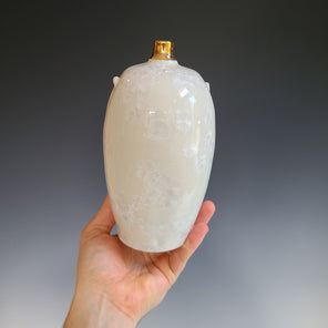 An ivory ceramic vessel with faux handles and a narrow gold luster neck.