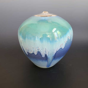 A porcelain sculptural vase with narrow opening. The vase has a multi layer glaze of greens, blues and 14k luster around the mouth of the vessel.  