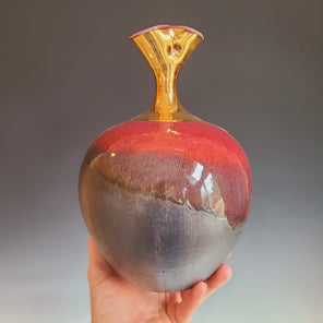 A red and dark umber glazed ceramic vessel with a gold neck.