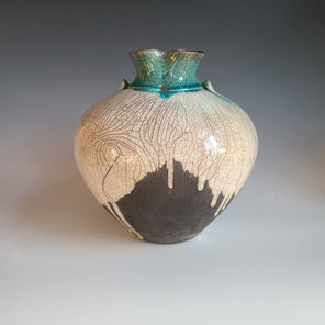 A textured white and charcoal grey glazed vessel with two small faux handles and a teal opening sits on a white surface.