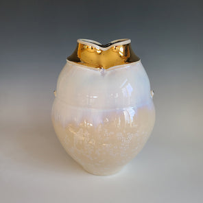 A white and cream crystalized glazed vase with two faux handles with a gold and white opening sits on a white surface.