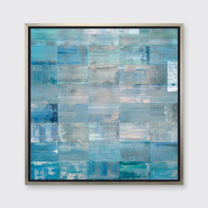 A blue and teal geometric print by Ned Martin in a silver floater frame hangs on a white wall.