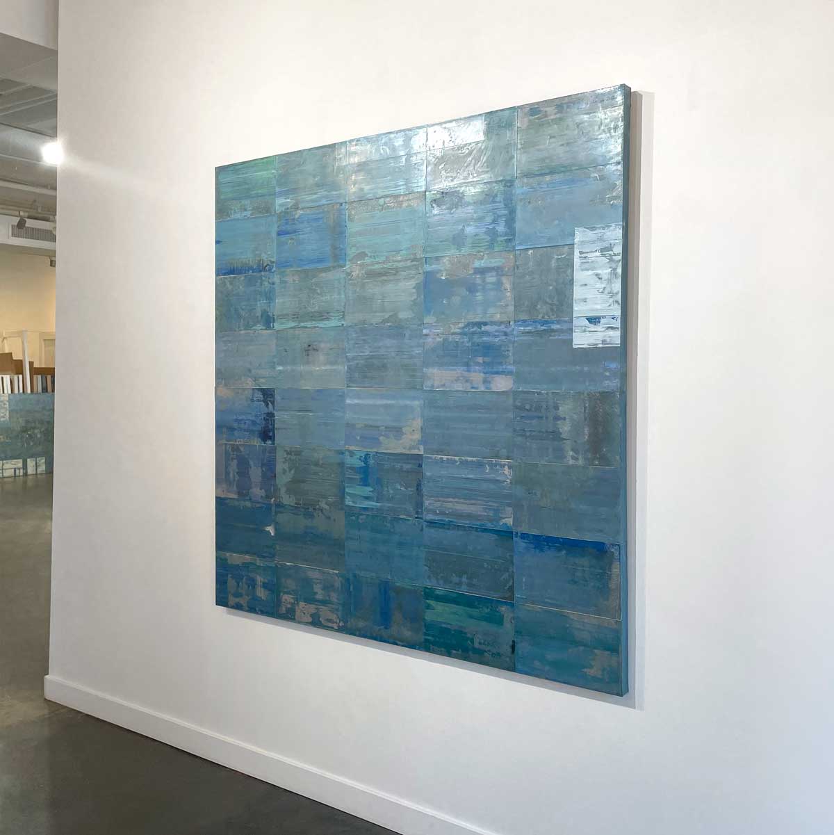 An abstract grid painting with a blue and green wash by Ned Martin hangs on a white wall with a view from the right. 