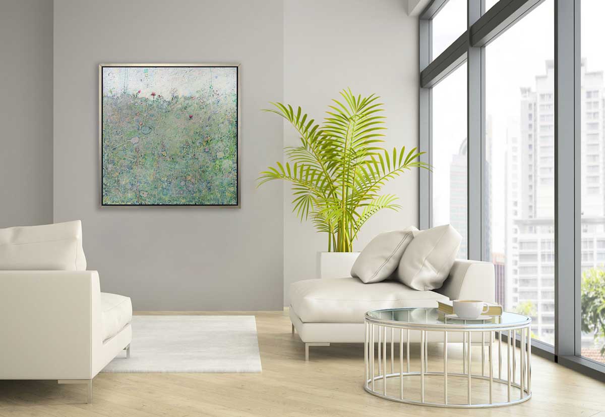 A green abstract landscape print in a silver floater frame hangs on a white wall across from two white sofas and a round glass top coffee table.