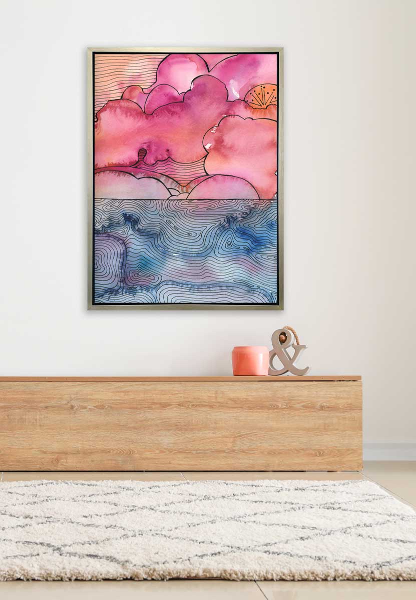A pink, blue and black abstract landscape print in a silver floater frame hangs on a white wall above a low wood bench with a peach candle and a ampersand decoration.