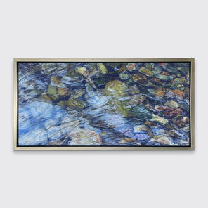 An abstracted riverbed print in a silver floater frame hangs on a white wall.