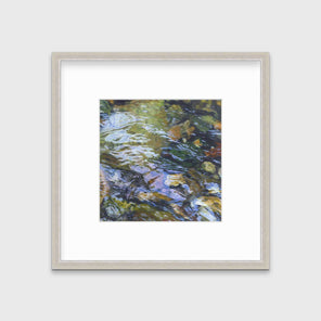 A green, brown and beige abstract river rock in water print in a silver frame with a mat hangs on a white wall.