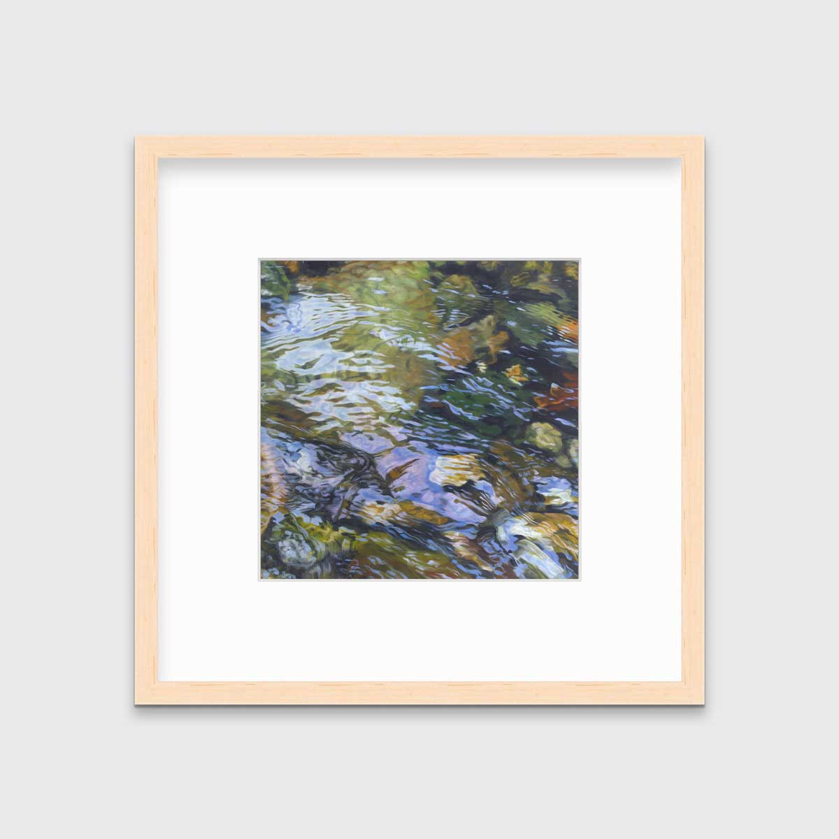 A green, brown and beige abstract river rock in water print in a natural wood frame with a mat hangs on a white wall.