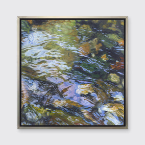 A green, brown and beige abstract river rock in water print in a silver floater frame hangs on a white wall.