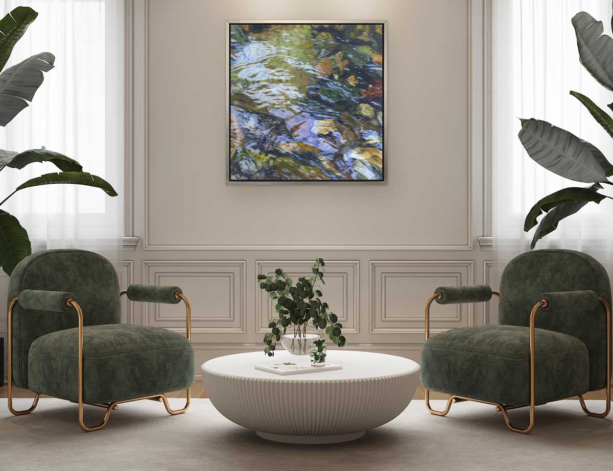 A green, brown and white abstract river rock print in a black floater frame hangs on a beige paneled wall above a low white round coffee table in between two green and gold chairs.