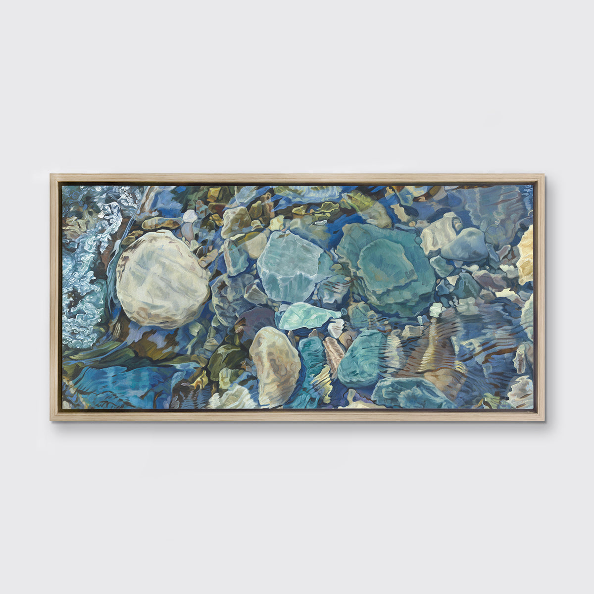 Abstracted print of grey, brown, green and beige river rocks under water hangs in a white oak wood floater frame on a white wall.