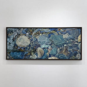 An oil painting of river rocks hangs on a white wall.