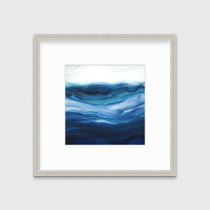 A blue, teal and white abstract print in a silver frame with a mat hangs on a white wall.