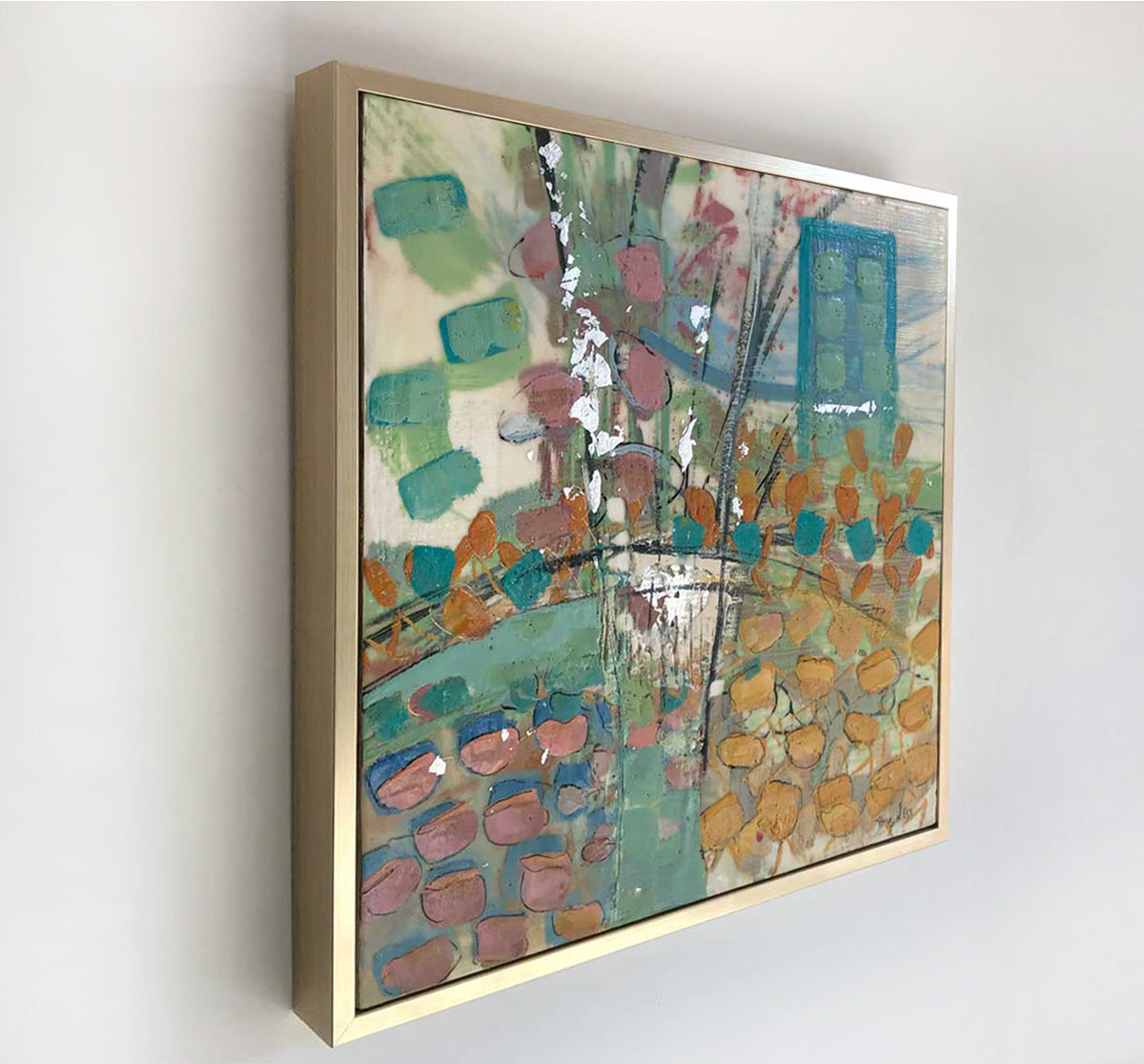 A left-hand, side-angle view of a nature-inspired multicolored abstract painting, framed in a gold frame hanging on a white wall. 