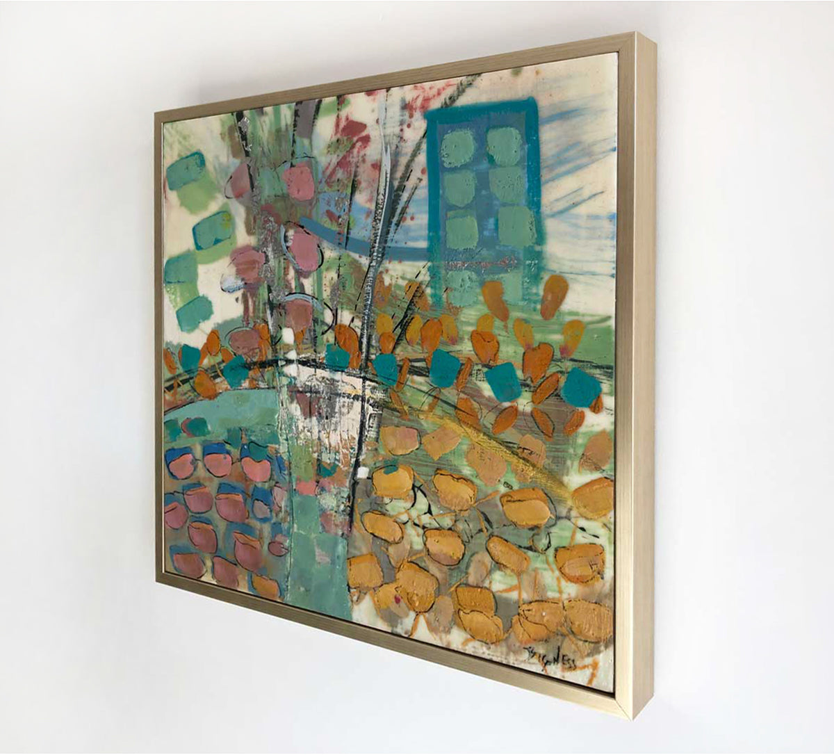 A right-hand, side-angle view of a nature-inspired multicolored abstract painting, framed in a gold frame hanging on a white wall.