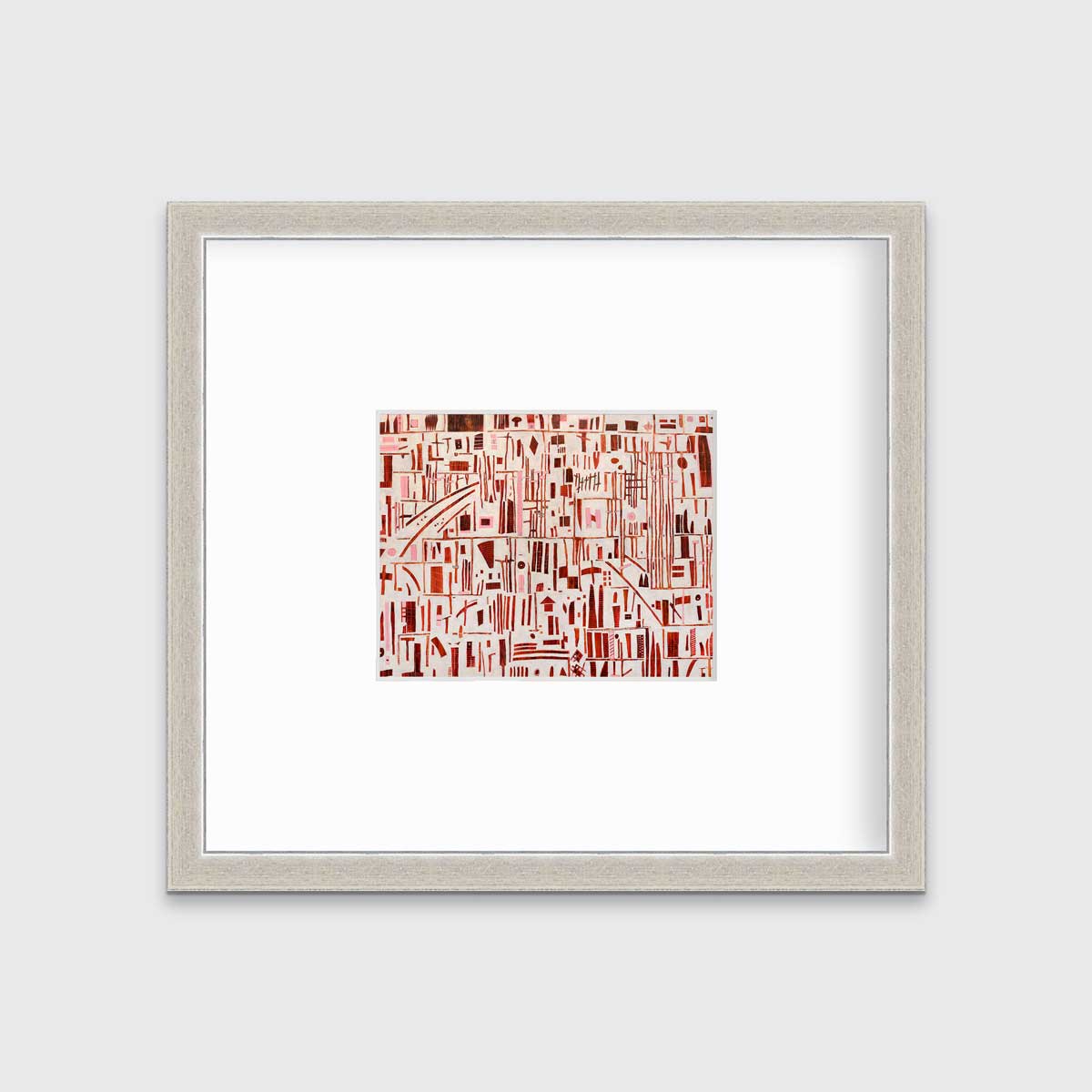 A red, pink and white abstract print in a silver frame with a mat hangs on a white wall.