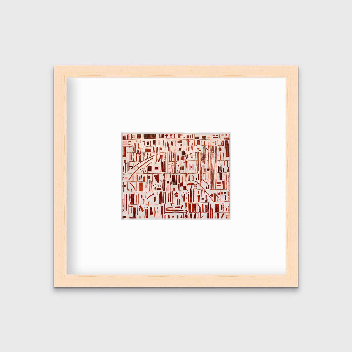 A red, pink and white abstract print in a natural wood frame with a mat hangs on a white wall.