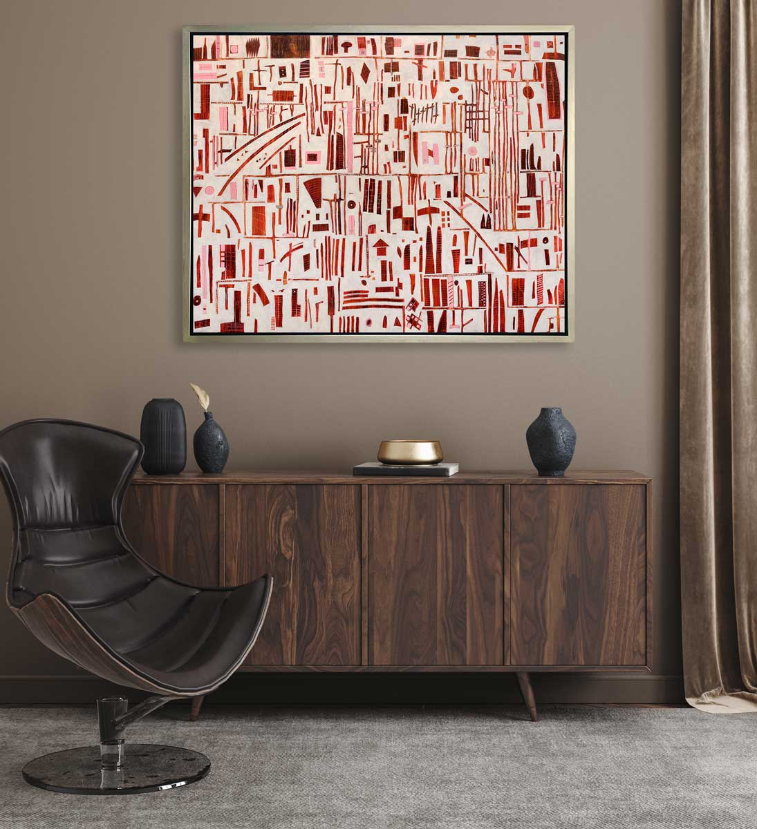 A red, pink and white abstract print in a silver floater frame hangs on a beige wall above a stained dark wood console cabinet with black vases, a gold decorative bowl and a brown modern chair.