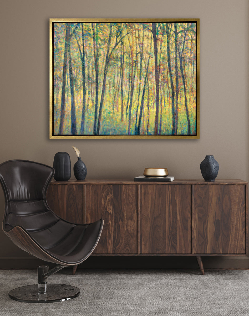 A yellow, brown and green abstract tree landscape print in a gold floater frame hangs on a beige wall above a dark wood cabinet with black vases, a gold decorative dish and a black modern chair.