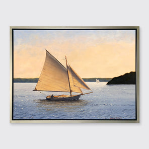A blue, beige and green seascape print with sailboats in a silver floater frame hangs on a white wall.
