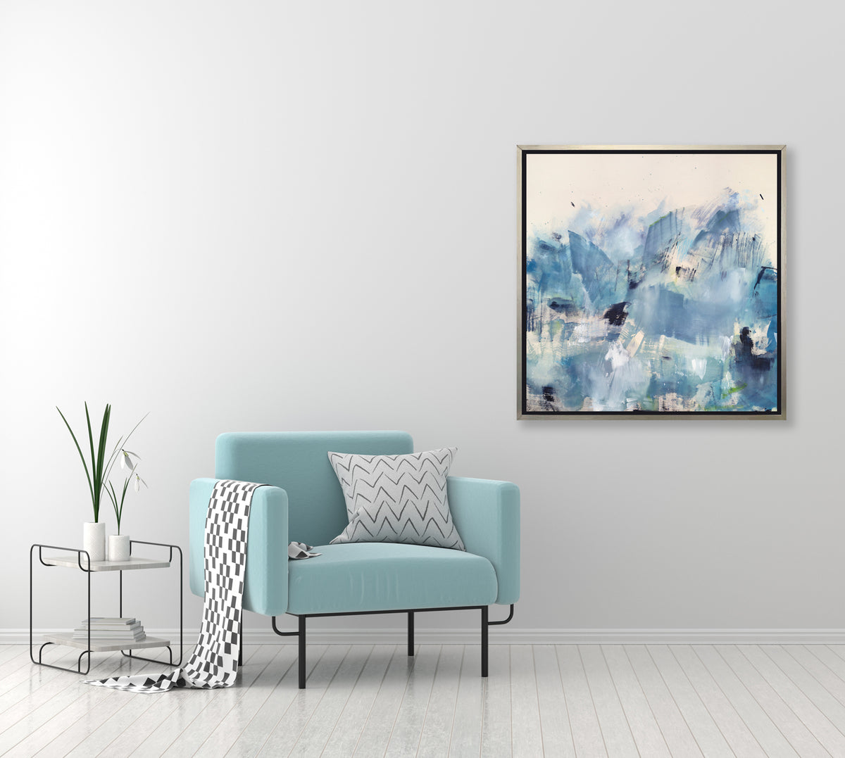 A blue and white abstract print hangs on a wall above a turquoise armchair and modern end table. 