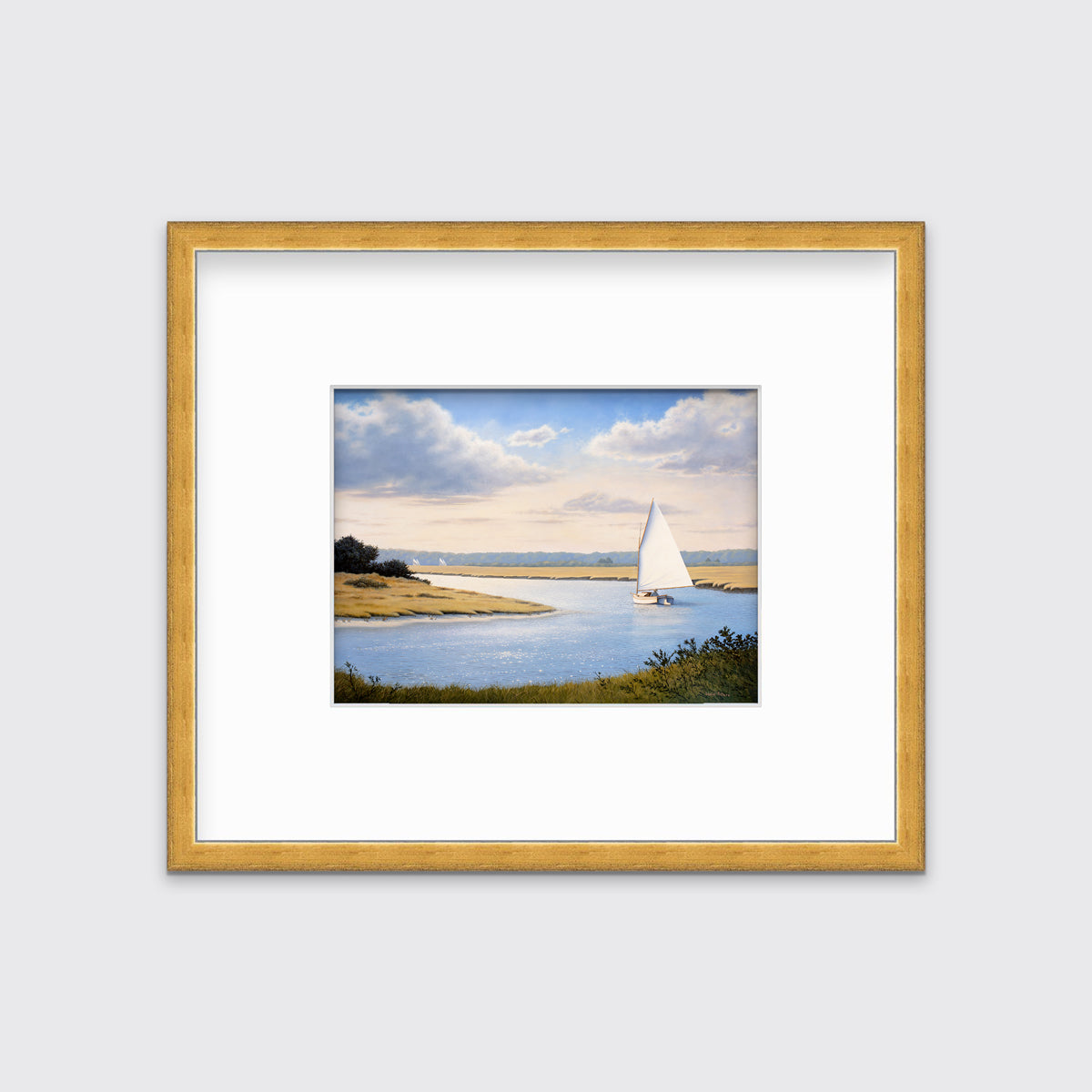 A print of a sailboat going down a winding blue river in a gold frame and mat hangs on a white wall.