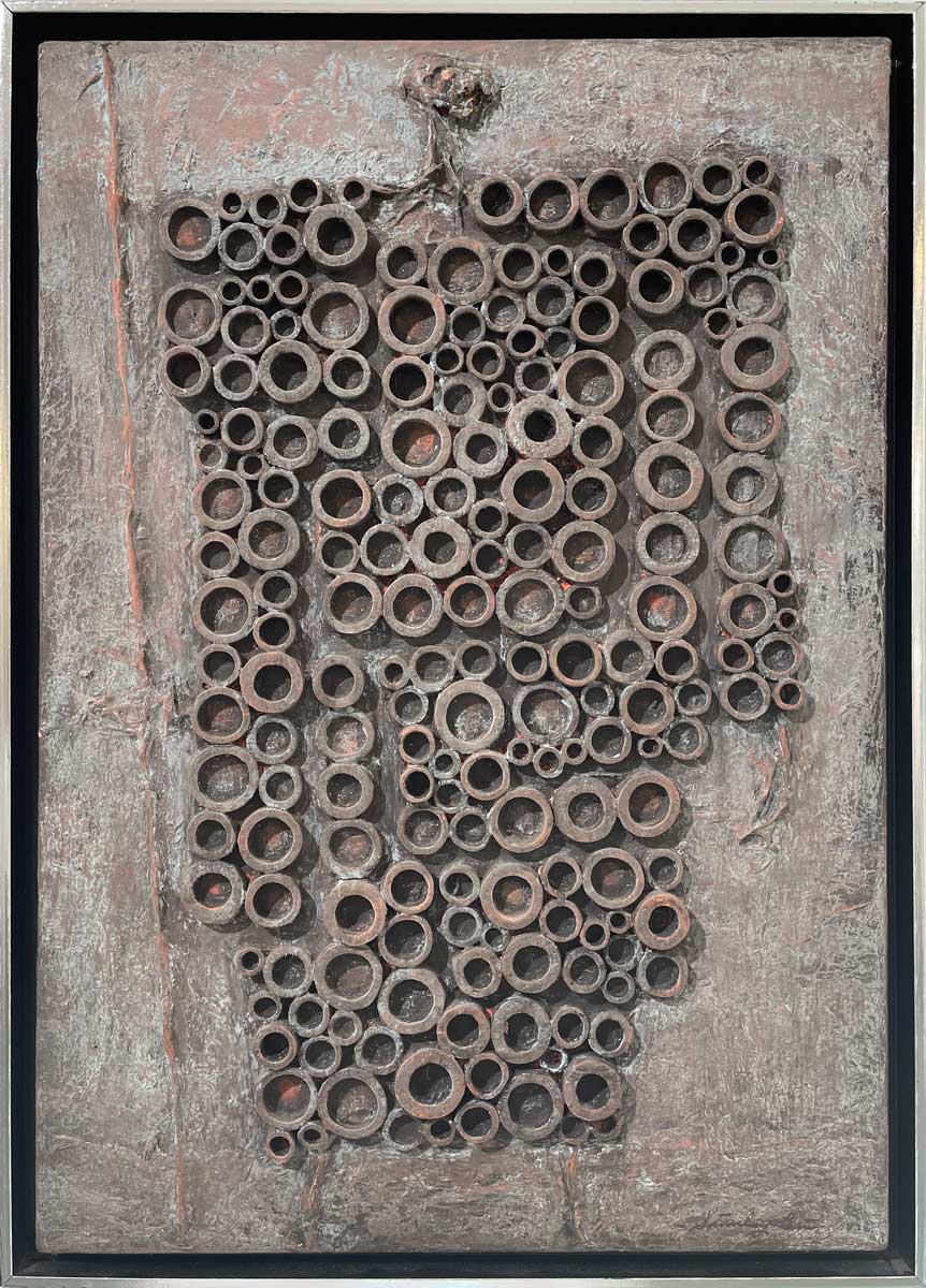 A grey and light rust orange abstract painting with embedded wood circles in a silver floater frame.