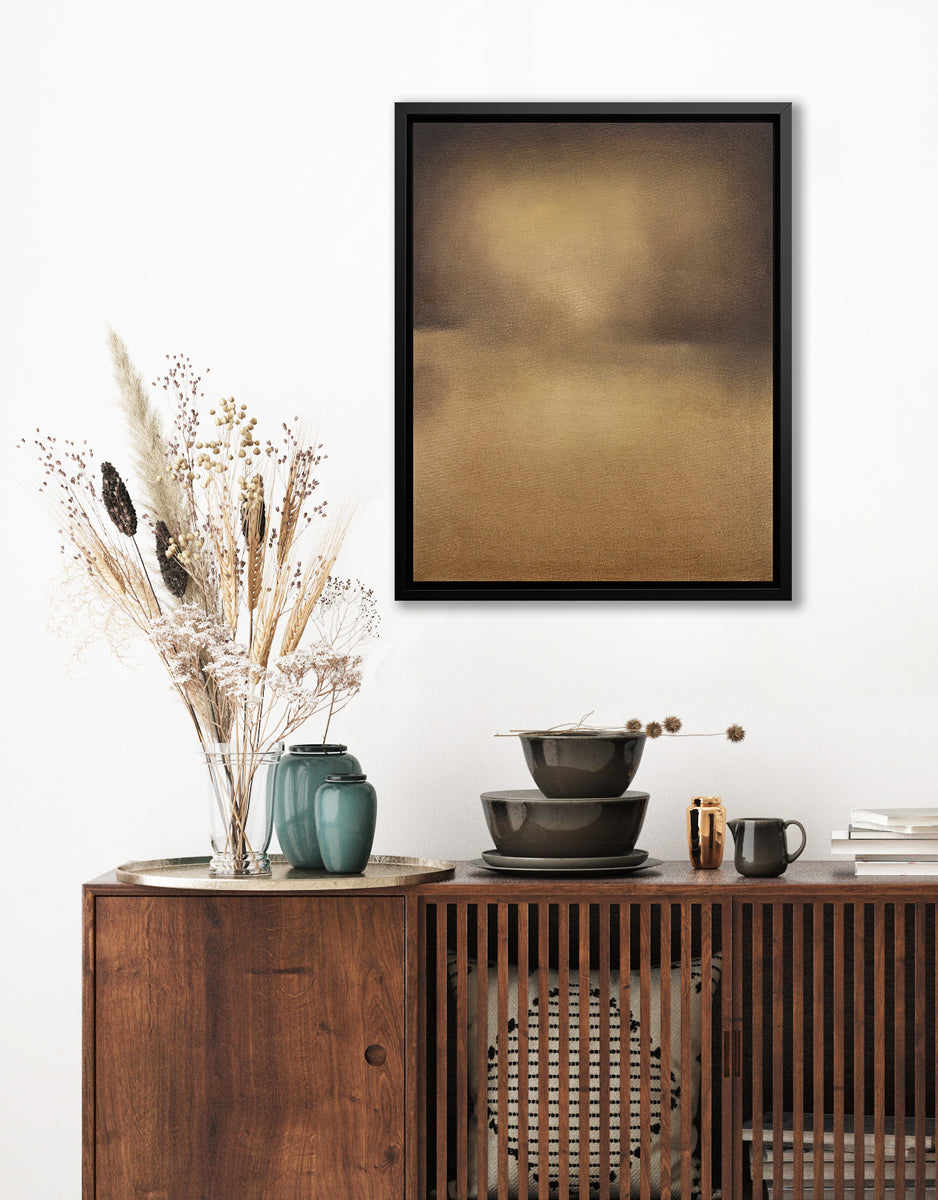 A brown and gold abstract print in a black floater frame hangs on a white wall above a dark wood credenza with a stack of brown bowls, a stack of books and a gold tray with two teal vases and a glass vase with wheat stems.