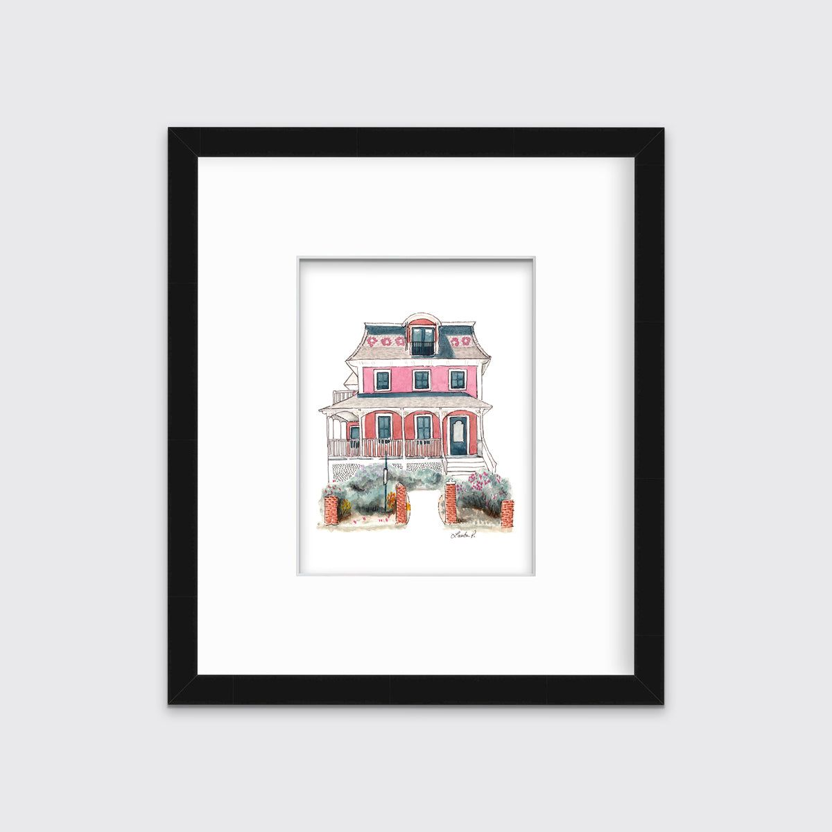 A pink and red house print in a black frame with a mat hangs on a white wall.