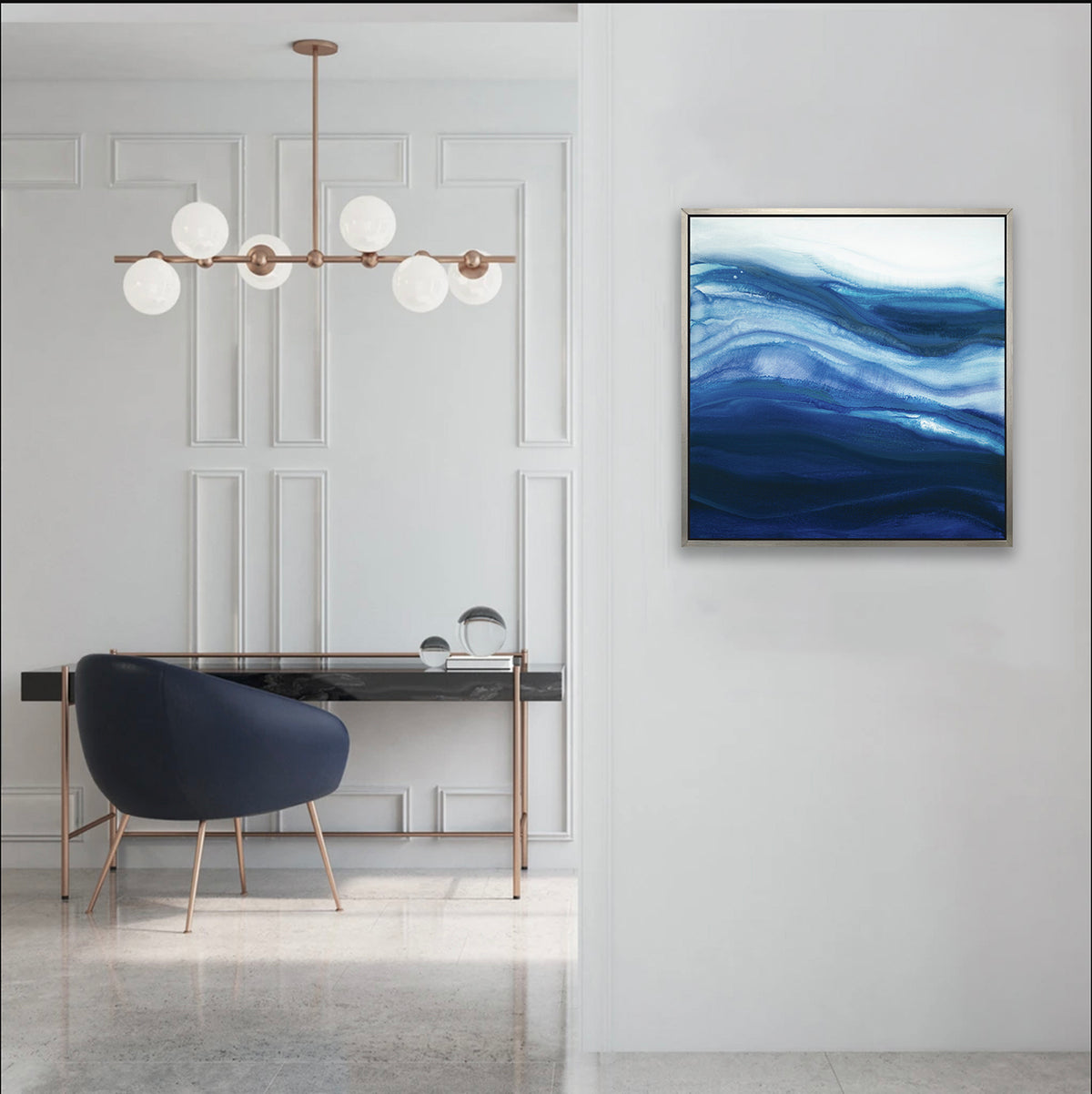 A blue, teal and white abstract print in a silver floater frame hangs on a white wall next to an opening to a room with a black marble desk and a navy modern chair.