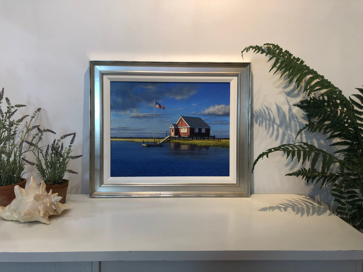 "Seaman Bay House" in a silver frame. Sitting on a white counter and resting on a white wall. 