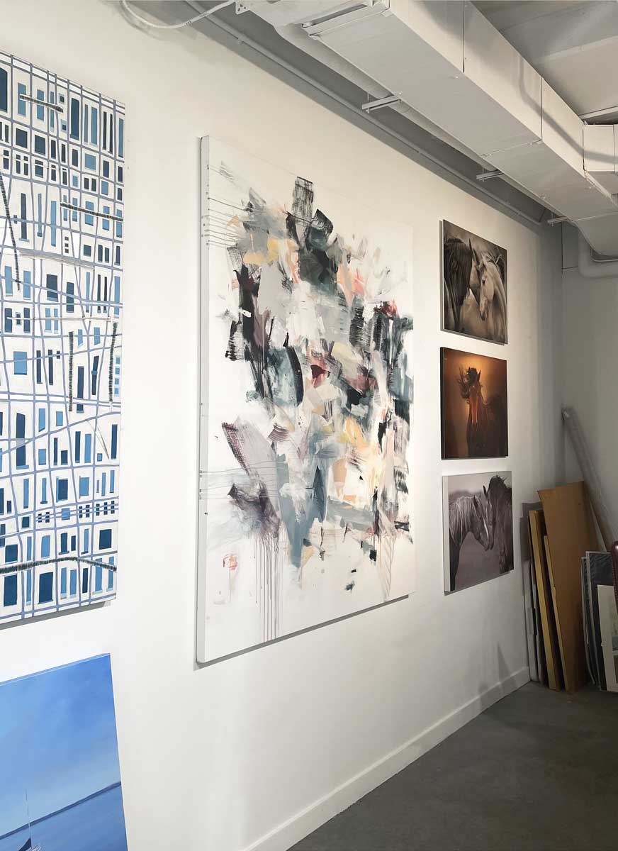 Multi-colored cool toned abstract painting by Kelly Rossetti hangs on a white wall in the gallery, viewed from the left. 
